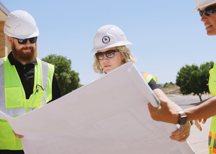 Performance Services team members in safety vests and hard hats looking at construction plans