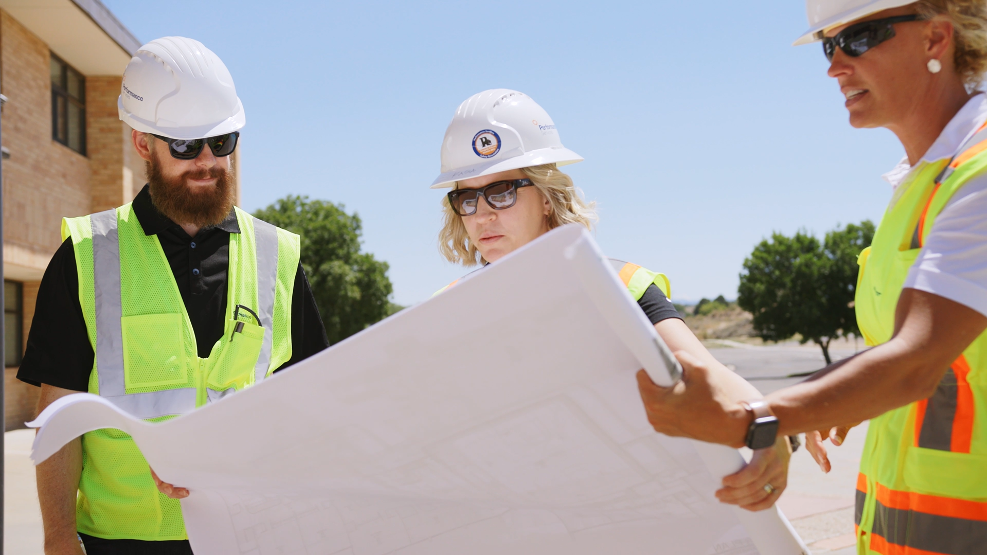 Performance Services team members in safety vests and hard hats looking at construction plans
