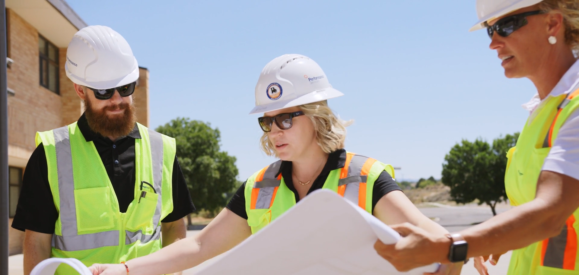 Performance Services team members in safety vests and hard hats looking at construction plans