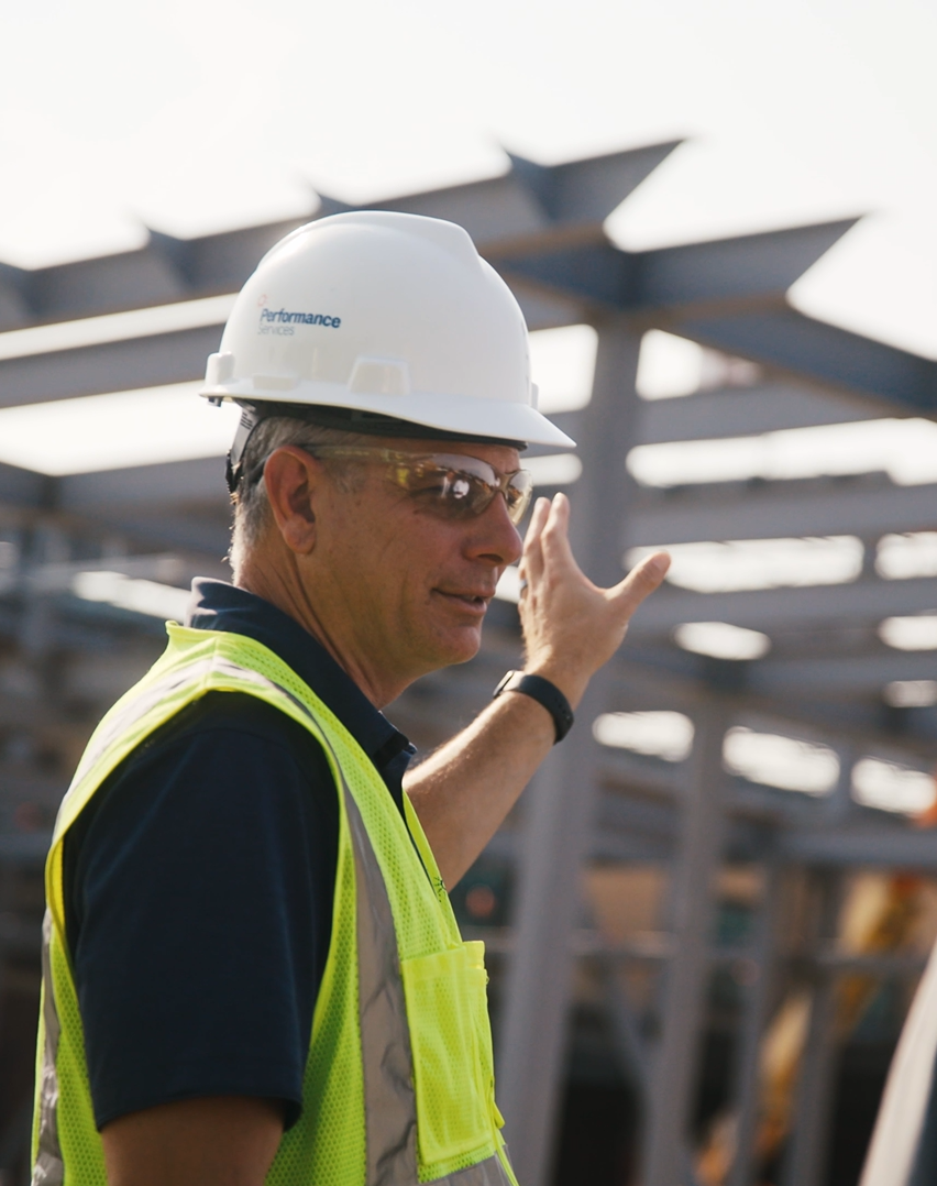 Performance Services Project Manager in a hard hat and safety vest talking to a client at a jobsite