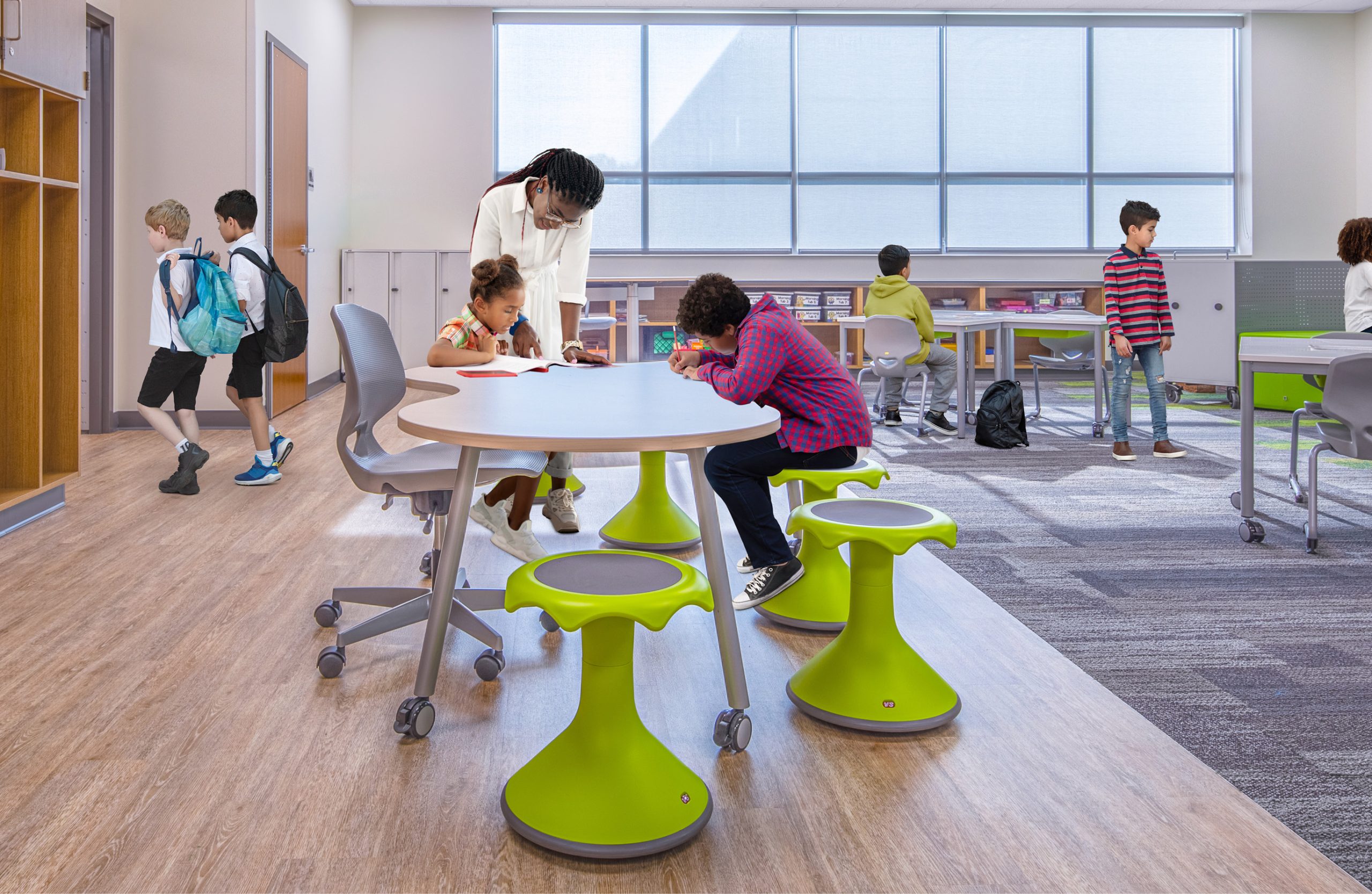 Students working on a project at a table in a classroom with a teacher helping